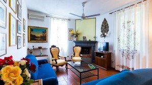A living room with a blue sofa, a chair, a coffee table, and a fireplace. There are framed pictures on the wall and a ceiling fan.