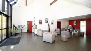 Een ruime lobby met een hoge plafond, grote ramen en diverse zithoeken.