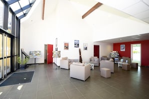 Eine geräumige Lobby mit hoher Decke, großen Fenstern und verschiedenen Sitzbereichen.