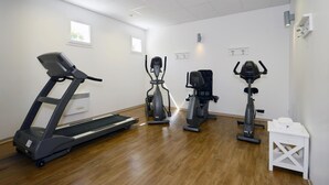 Een fitnessruimte met loopband, elliptische trainer en hometrainers.