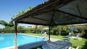Un espace piscine doté d’un coin salon couvert, de chaises longues et d’une table.