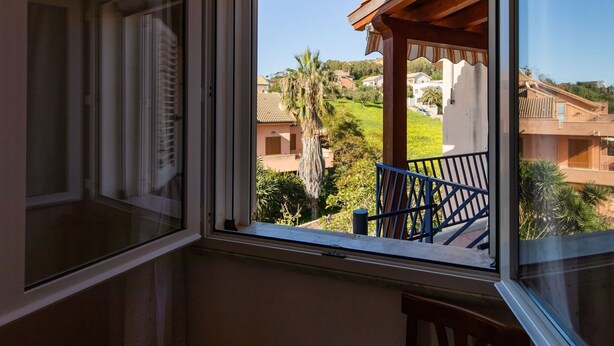 A room with a window overlooking a residential area, including houses and greenery.