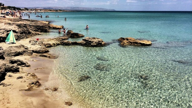 A beach with clear shallow waters, rocky areas, and a few people swimming. - Holiday Home near Mount Etna Views (Carlentini)
