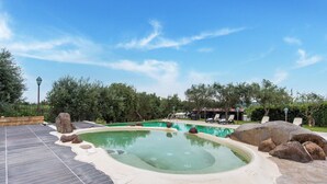 A swimming pool with a hot tub, surrounded by rocks and trees, and a covered area with lounge chairs. - Holiday Home near Mount Etna Views (Carlentini)