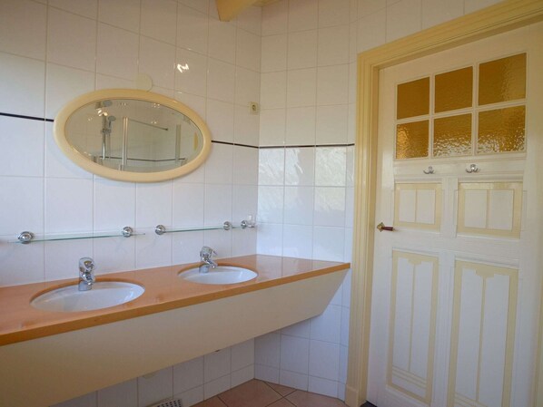 Un baño con dos lavabos, un espejo y una puerta con panel de vidrio.