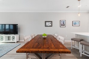 A dining area with a wooden table, chairs, a bowl of fruit, a television on a cabinet, and framed pictures on the wall.