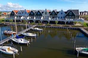 Traditional Dutch houses line the marina, connected by a walkway, with boats moored at the dock.