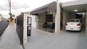 Ein weißes Auto steht in einer überdachten Garage neben einem Einfriedungsmauer umgebenden Haus mit einem Balkon.