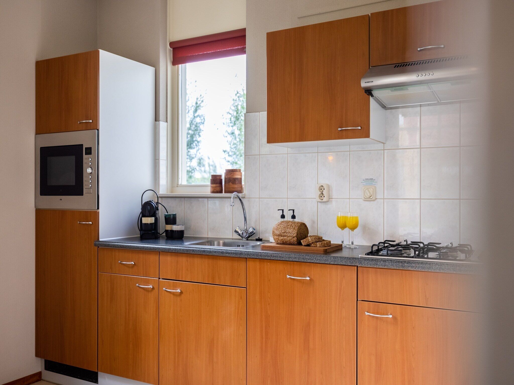 A modern kitchen with wooden cabinets, a built-in microwave, a gas stove, and a window with a view of trees.