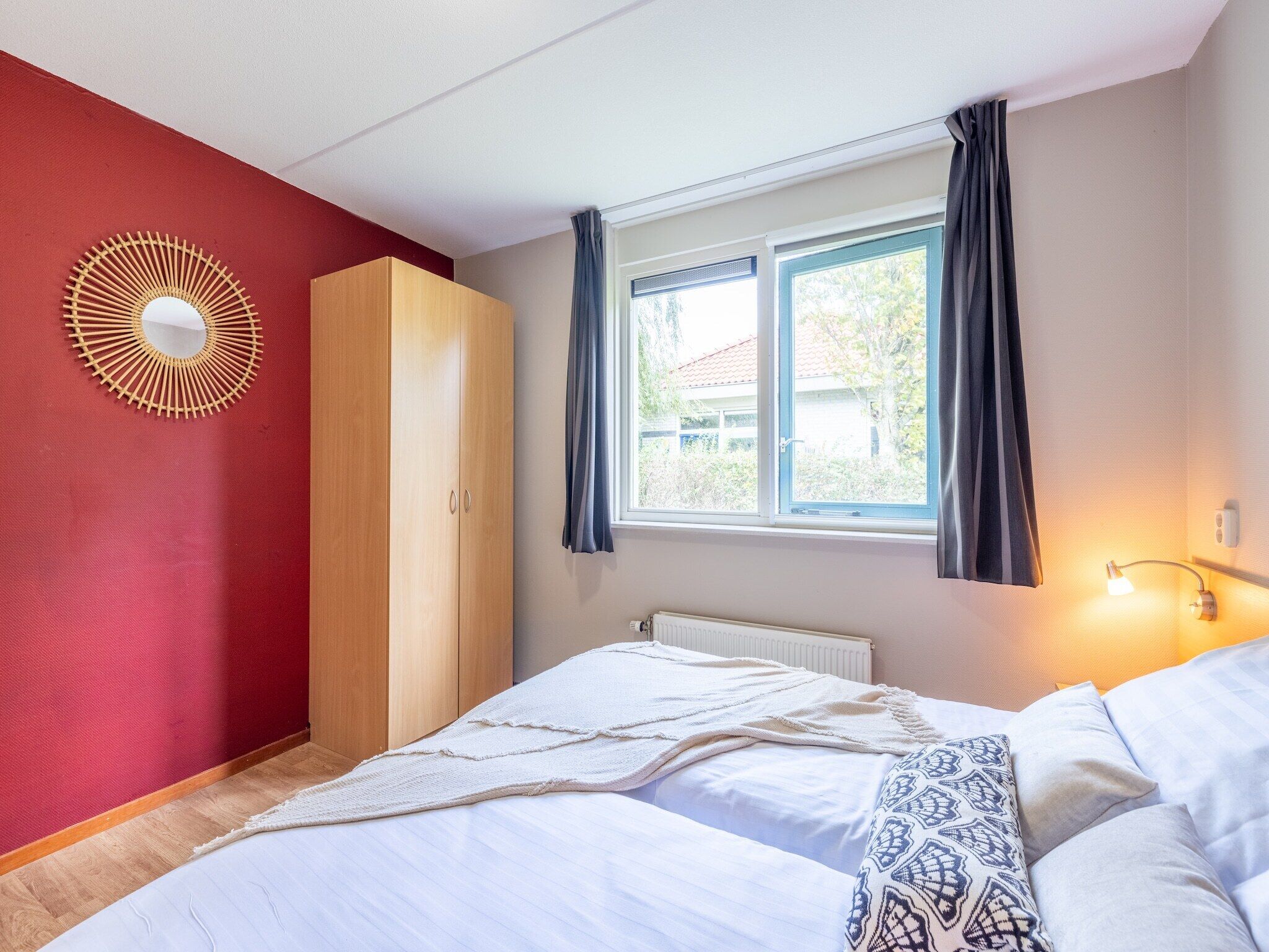 Une chambre à coucher comprenant un lit, une armoire, une fenêtre avec des rideaux et un luminaire fixé au mur.