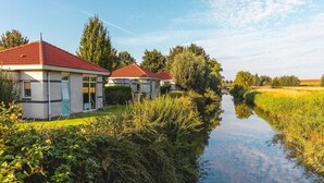 A canal-side building with a red roof and white walls, surrounded by lush greenery and a calm waterway.