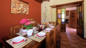 A dining area with a long wooden table set for a meal, a potted plant with pink flowers, and a decorative wall piece.