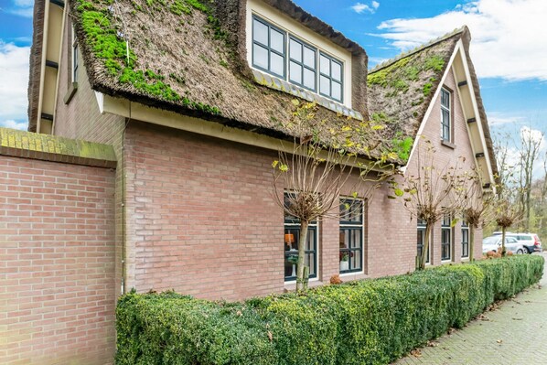 A traditional brick house with a thatched roof and a well-maintained hedge along the sidewalk.