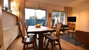 Un coin repas avec une table et des chaises en bois, un saladier de fruits et un téléviseur posé sur un meuble.