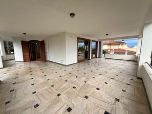 A spacious balcony with a tiled floor, large sliding glass doors, and a view of a residential area.