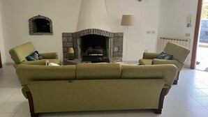 Een woonkamer met een stenen openhaard, twee fauteuils, een bank en een lamp.