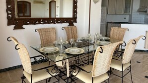 Een eetruimte met een glazen tafel, rieten stoelen en een grote, decoratieve spiegel.