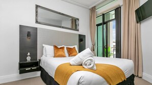 Une chambre d’hôtel avec un lit, une table de chevet, un miroir et une fenêtre avec des rideaux.