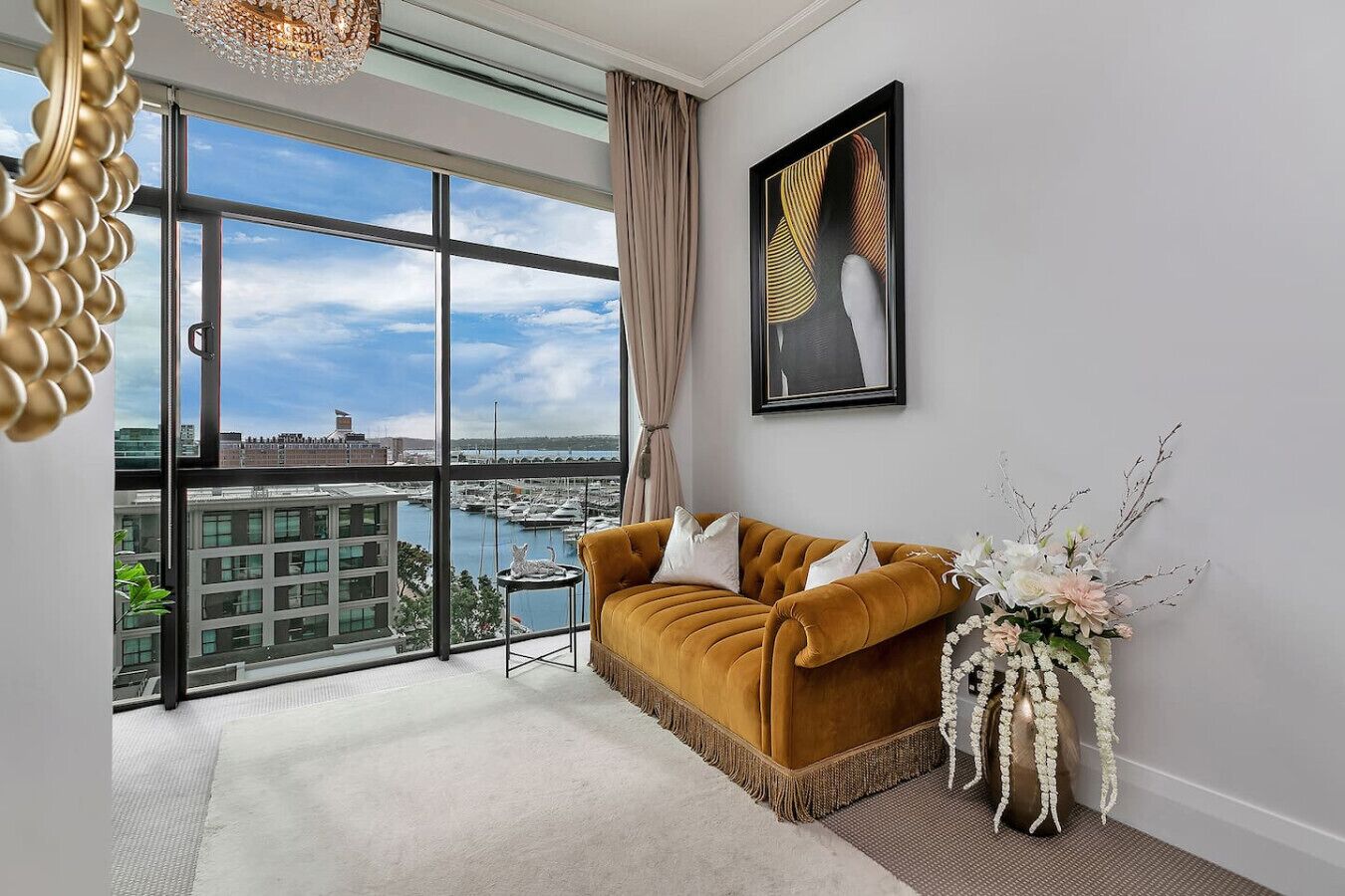 A modern living room with a large window, a sofa, a decorative vase, and a framed artwork.