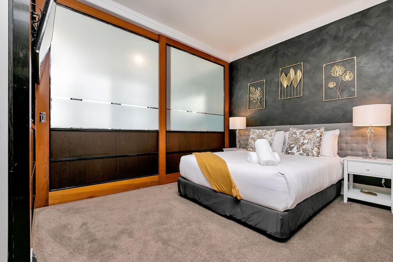 A bedroom with a bed, nightstands, a lamp, a large window with frosted glass, and wall art.