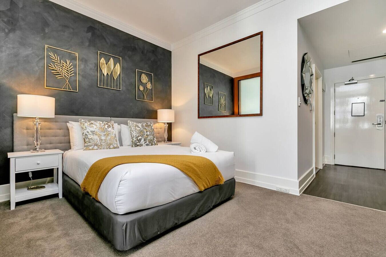 Une chambre à coucher moderne avec un grand lit, une table de chevet, un miroir et des œuvres d’art accrochées au mur.
