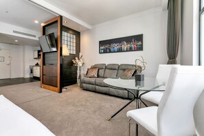 A modern living room with a sofa, a glass coffee table, and a dining area with a white chair.