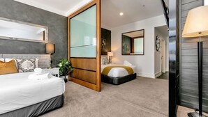 A hotel room with a bed, bedside table, lamp, and a sliding door leading to another room.