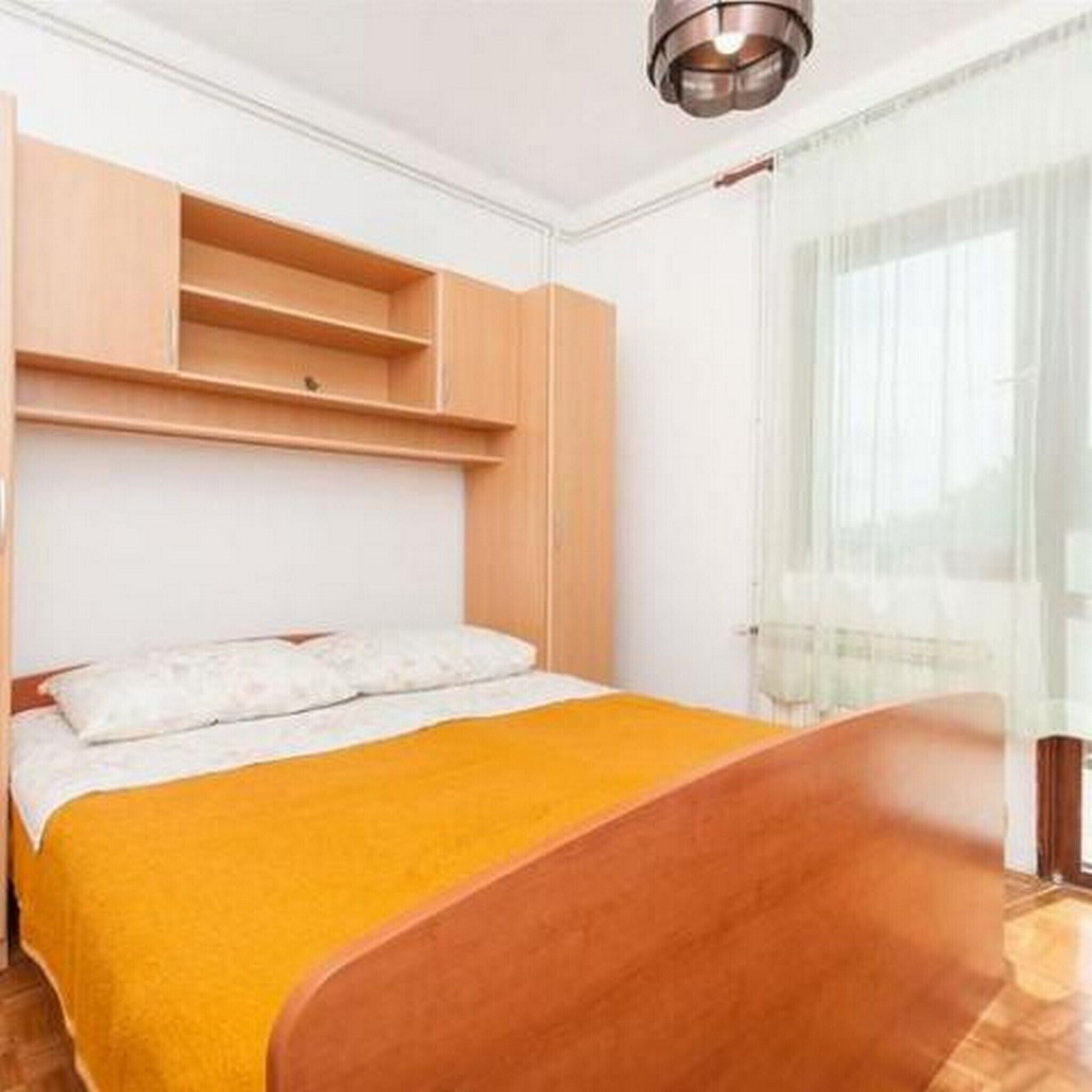 A bedroom with a bed, a wooden headboard, a bedside table, and a window with sheer curtains.