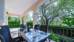 Un área de comedor al aire libre cubierta con una mesa y sillas de vidrio, rodeada de follaje y vistas a árboles.