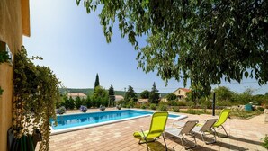 Una piscina con un borde de baldosas, rodeada de sillas verdes y plantas.