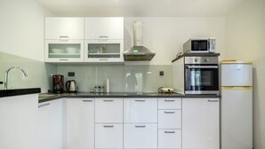 Una cocina moderna con armarios blancos, una campana extractora de acero inoxidable, un microondas integrado y un refrigerador.