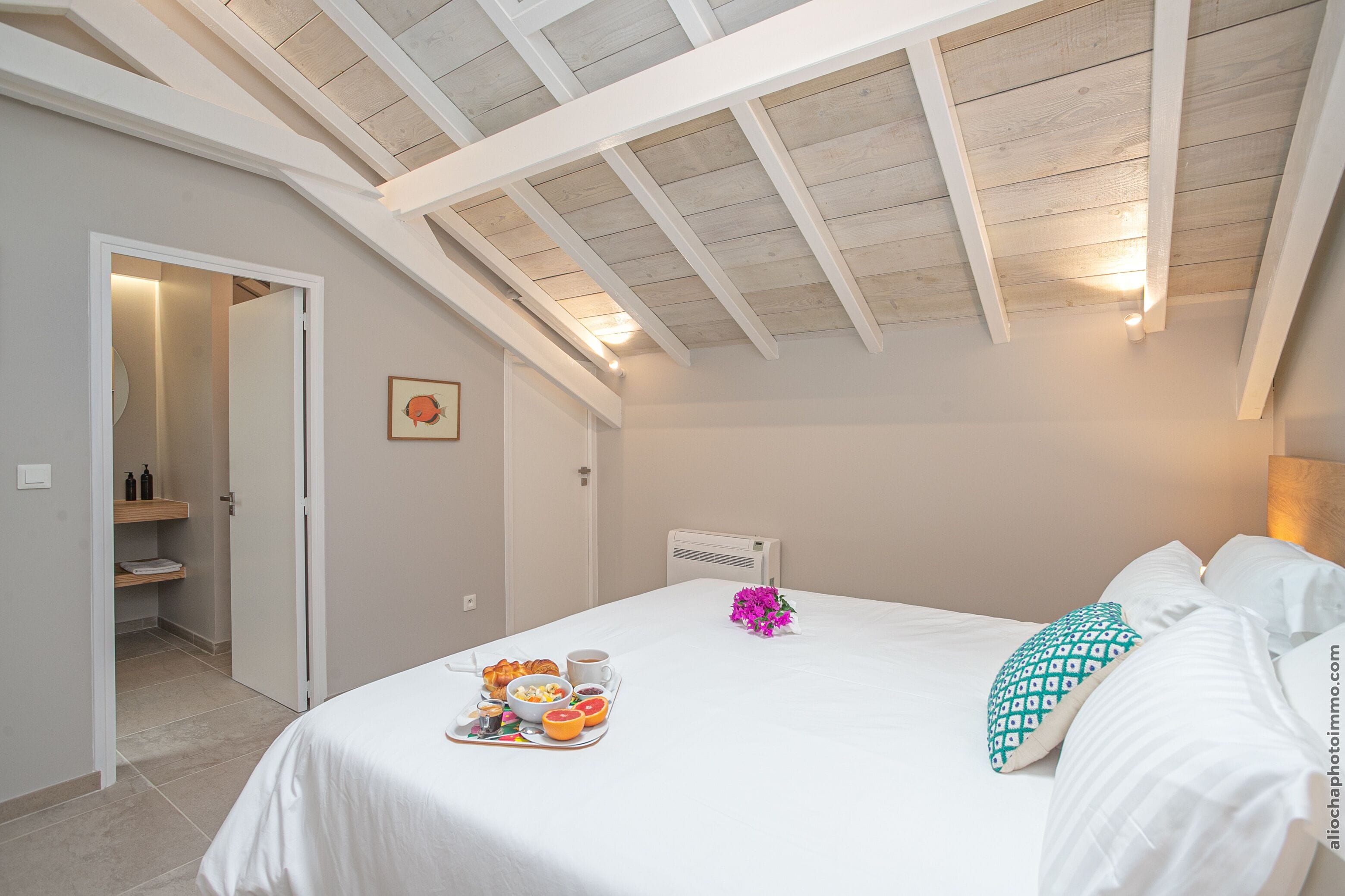 A bedroom with a sloped ceiling, a bed with white bedding, a tray with breakfast items, and a small vase of flowers.