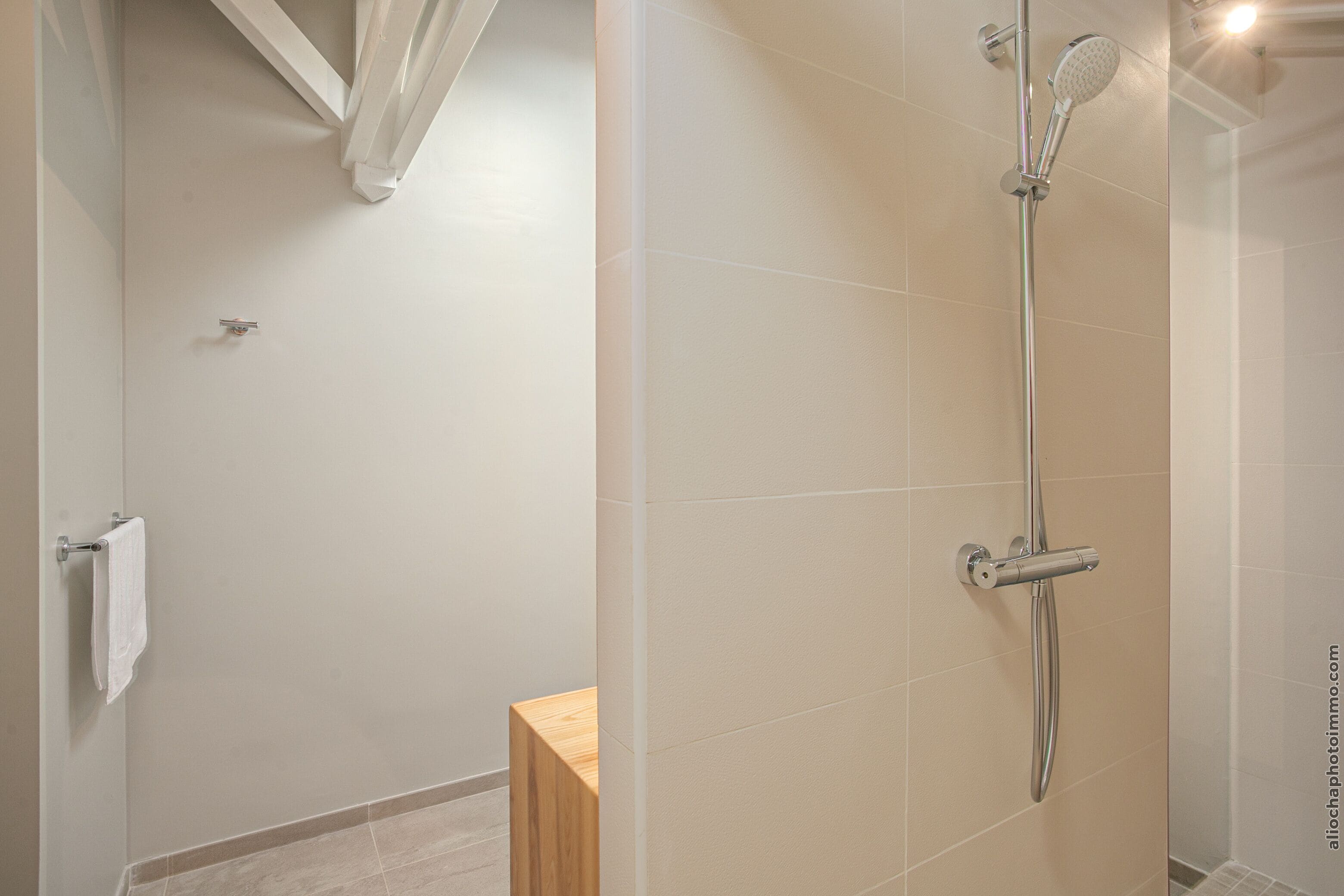 A modern bathroom with a shower, a wooden stool, and a towel rack.