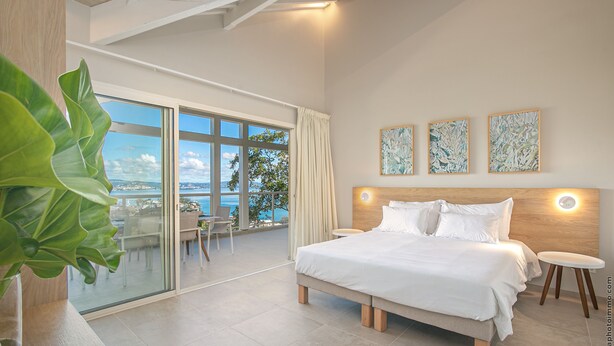 Une chambre à coucher moderne avec un grand lit, un balcon offrant une vue dégagée et trois tableaux abstraits accrochés au mur.