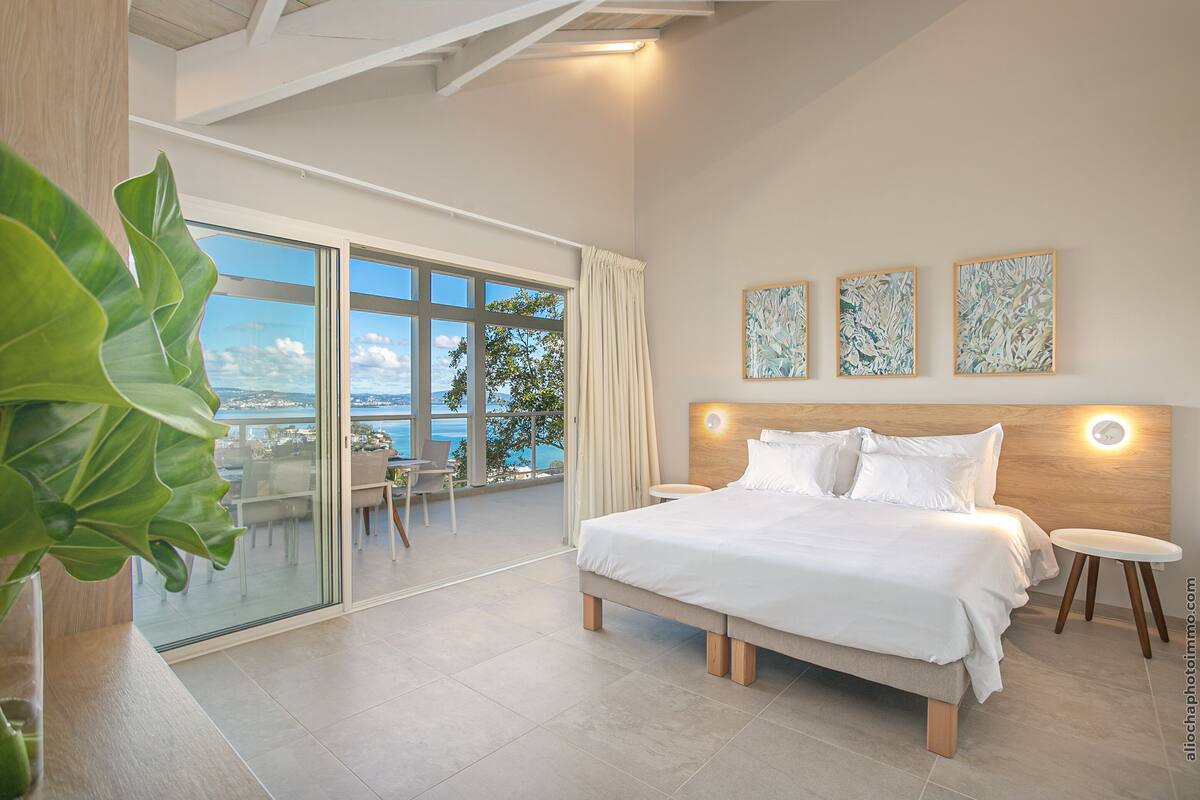 Un dormitorio moderno con una cama grande, un balcón con vistas y tres cuadros abstractos en la pared.