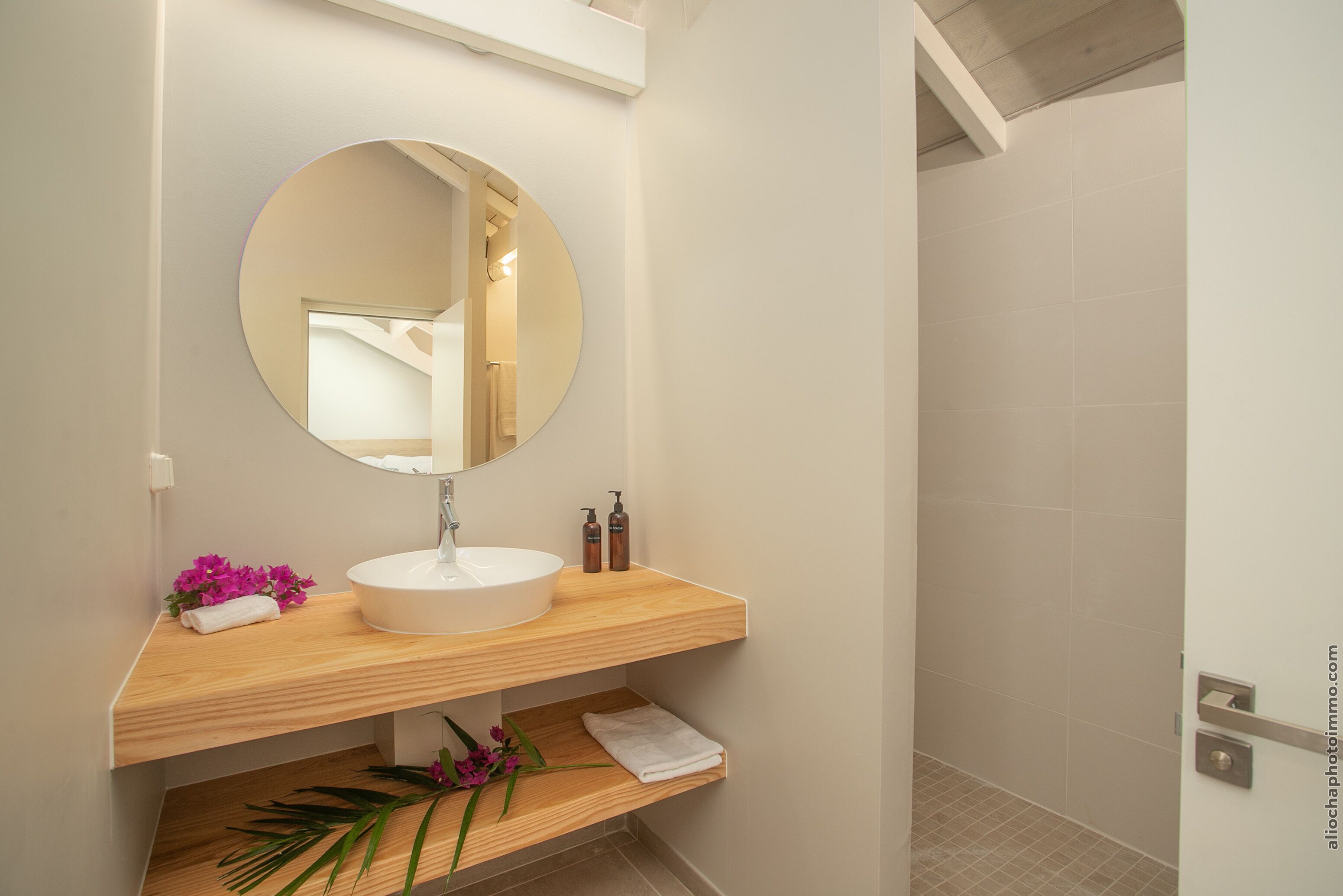A bathroom with a round mirror, wooden vanity, and a shower area.