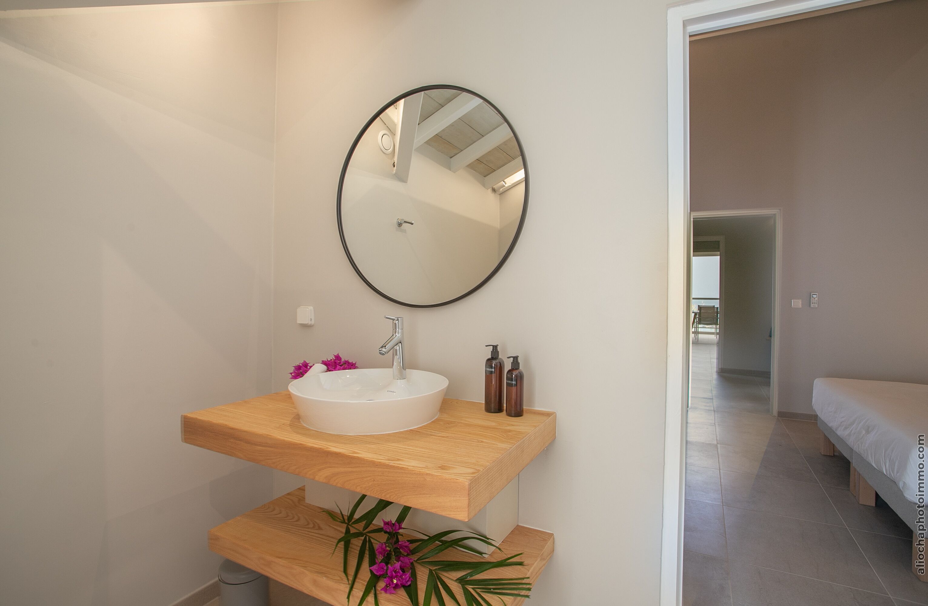 A modern bathroom with a wooden vanity, a round mirror, a white sink, and a small plant.