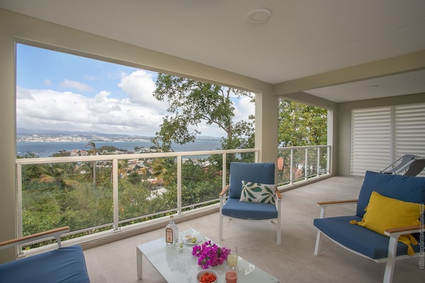 A balcony with a view of the sea and cityscape, furnished with a table, chairs, and a bottle. - Tangarane (Trois-Ilets)