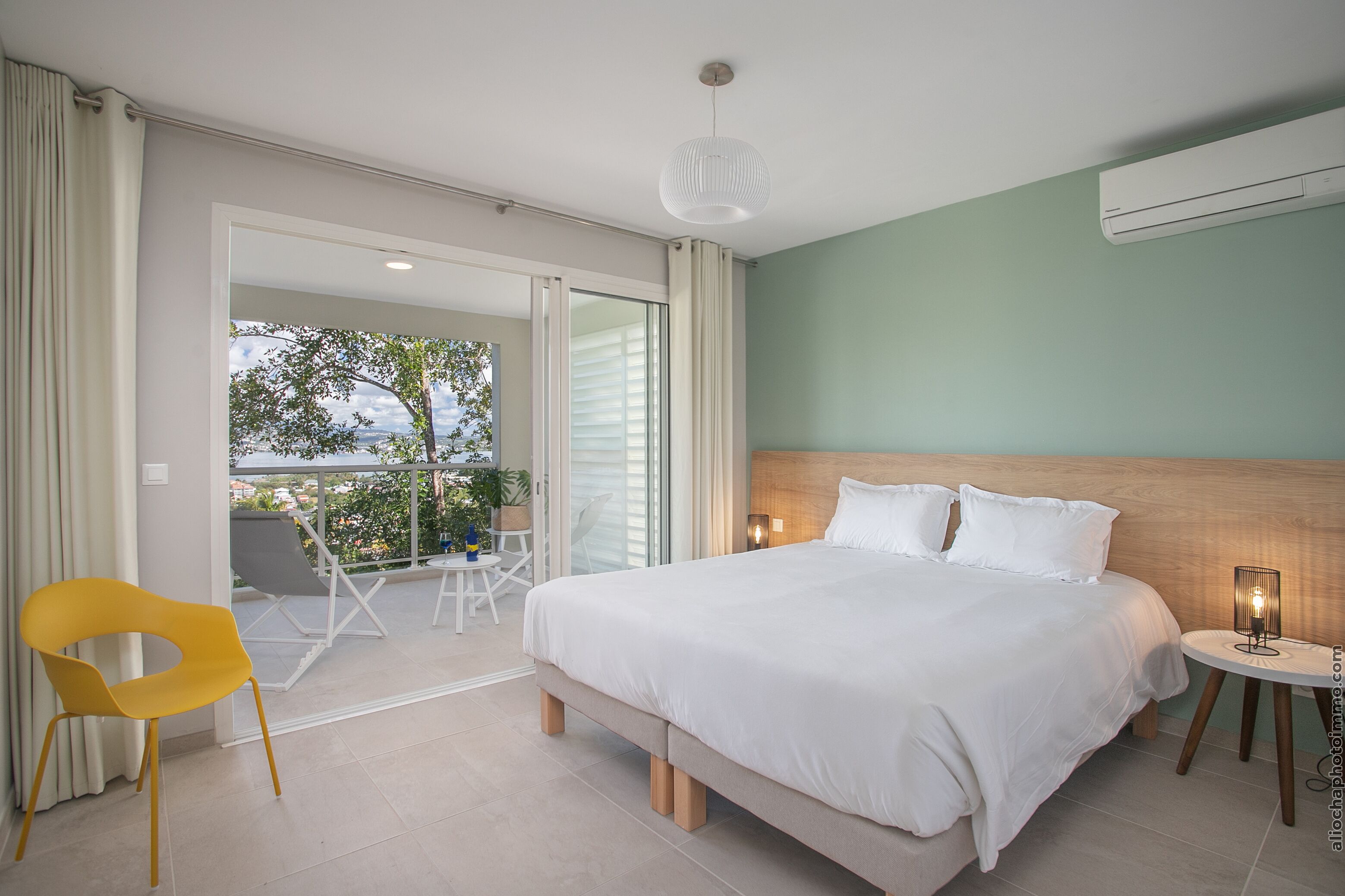 Un dormitorio con una cama grande, una mesita de noche con lámpara, una silla y vistas al exterior.