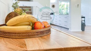 Ein Korbrand-Obstkorb steht auf einem Holztisch in einer modernen Küche mit weißen Schränken und einer sichtbaren Treppe.