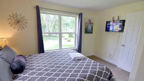 Une chambre avec un lit, une fenêtre avec des rideaux, un téléviseur fixé au mur et une porte.