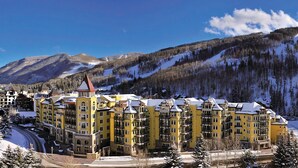 A large yellow hotel with multiple floors and a prominent tower, surrounded by snow-covered mountains and trees. - Beautiful Resort in Vail Colorado (Vail)