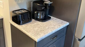 Una cocina compacta con armarios oscuros, una cafetera integrada y un tostador.