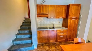 A kitchen with wooden cabinets, a sink, and a staircase leading to another level.