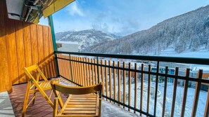 A wooden balcony with a view of snow-covered mountains and a river.