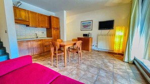 A compact living space with a kitchenette, a dining area, a TV, and a radiator.