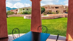 Une terrasse avec une table et des chaises, donnant sur une pelouse bien entretenue et une rangée de bâtiments aux toits de tuiles.