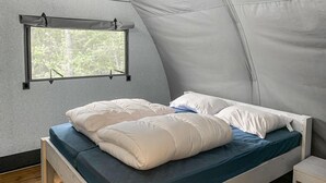 Una cama individual con ropa de cama blanca en una habitación tipo tienda con ventana.