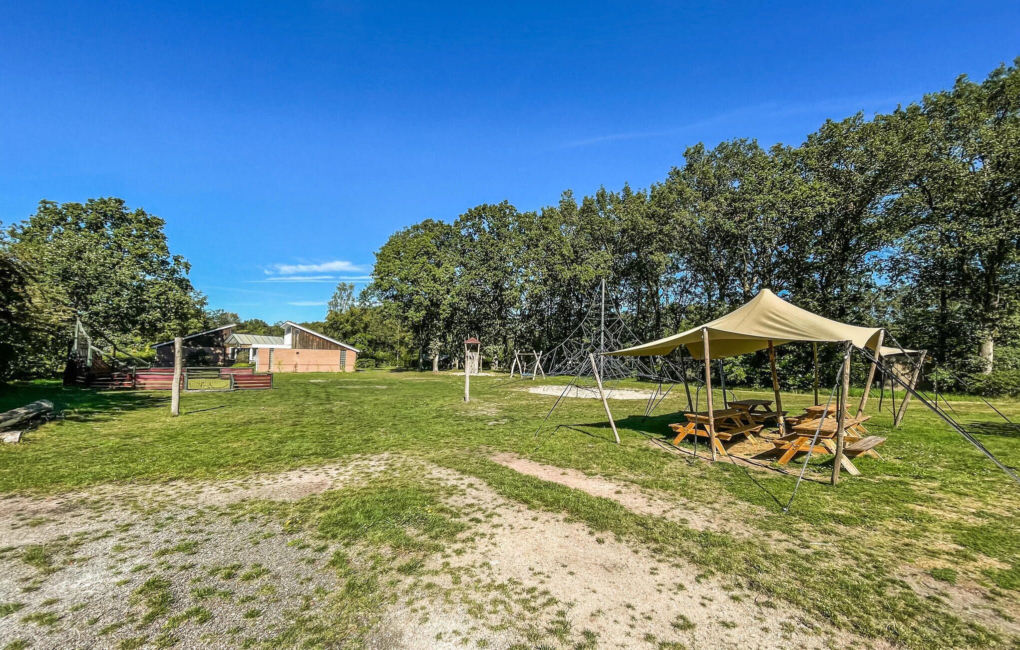 En campingplads med et telt, picnicborde og en lade i baggrunden.