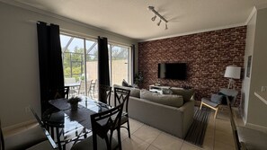 Relax in a spacious living area with a dining table, sofa, and TV, connected to an outdoor patio through a sliding glass door.